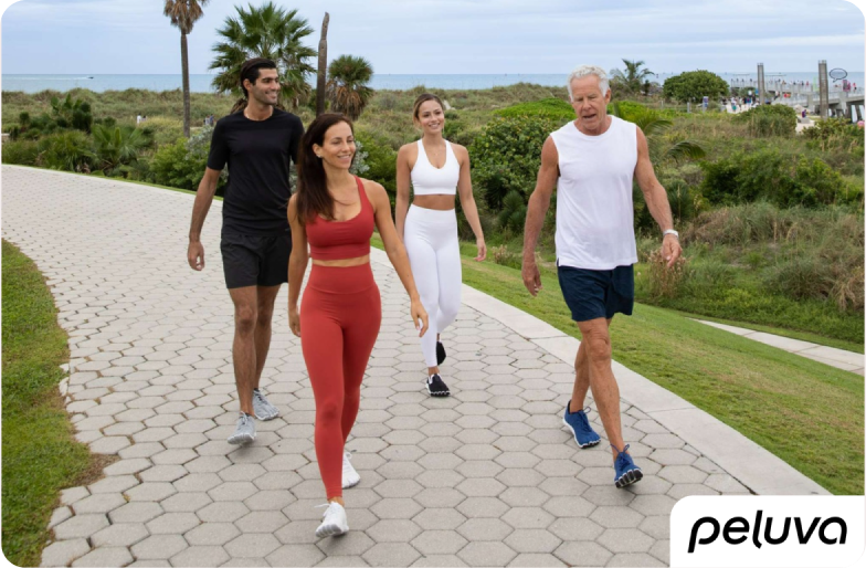 Four people of different ages and backgrounds walking together on a scenic paved path, dressed in activewear